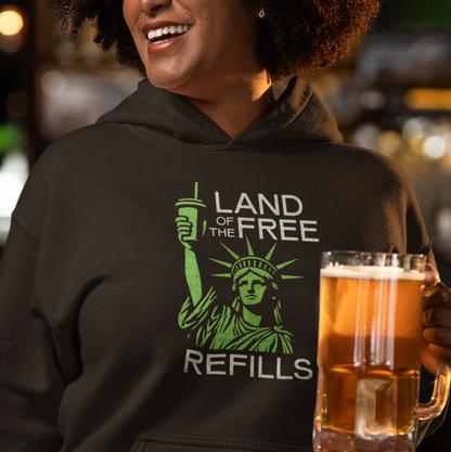 Person wearing a hoodie with 'Land of the Free Refills' design, holding a beer mug in a casual setting.